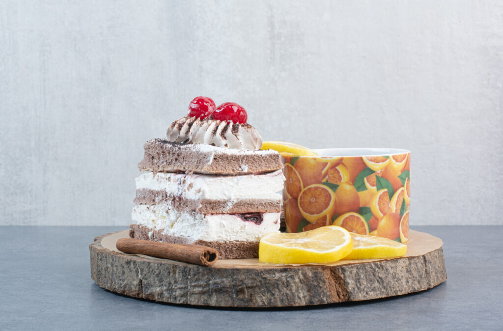 A piece of cake with sliced lemon and cinnamon stick on wooden board. High quality photo